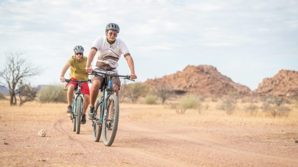a couple of people riding bikes down a dirt road